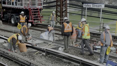 A-stationary-shot-of-several-men-working-on-the-Long-Island-Railroad-tracks,-wearing-fluorescent-vests-on-a-cloudy-day