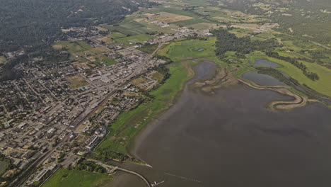 Salmon-Arm-BC-Canada-Aerial-v6-high-birds-eye-view-flyover-Shuswap-Lake-capturing-lakeside-town-center-and-residential-area,-tilt-up-reveals-mountain-landscape---Shot-with-Mavic-3-Pro-Cine---July-2023