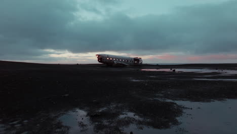 Drone-footage-of-the-abandoned-DC-Plane-on-the-black-sand-beach-of-Sólheimasandur,-Iceland,-captured-under-a-cloudy-sunrise-with-dark,-cinematic-tones