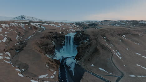 Skógafoss-waterfall-and-Skógá-River-in-southern-Iceland,-showcasing-a-snowy-landscape-under-cloudy-skies