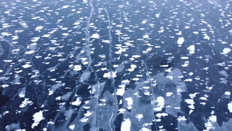 Looking-down-at-frozen-ice-from-above-and-tilting-up-to-reveal-snow-covered-Rocky-Mountains,-aerial