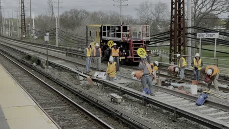 Una-Toma-Desde-El-Andén-De-La-Estación-De-Hombres-Que-Trabajan-En-Las-Vías-Del-Ferrocarril-De-Long-Island,-Con-Chalecos-Fluorescentes-En-Un-Día-Nublado.