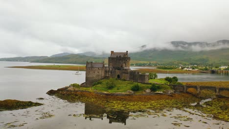 Pullback-Aerial-Angle-of-Eilean-Donan-Castle-on-Loch-Duich-in-the-Scottish-Highlands-on-Low-Tide,-Scotland,-United-Kingdom