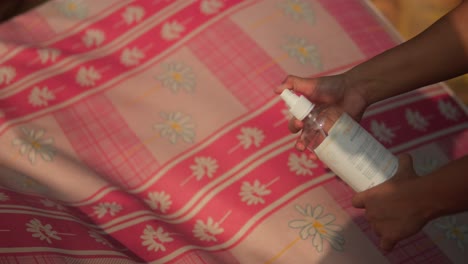 Unrecognizable-person-is-holding-a-spray-bottle-on-a-pink-and-white-cloth