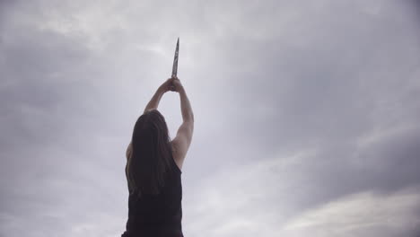 Empowered-woman-with-bare-arms-holds-sword-up-to-sky,-female-power