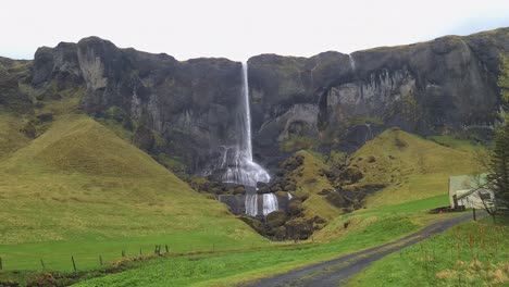 Landscape-of-Iceland,-Waterfall,-Volcanic-Cliffs-and-Green-Grassland-on-Rainy-Day