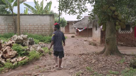 Tansania-Junge-Männliche-Fuß-Unbefestigten-Straßen-In-Ländlichen-Armen-Dorf-Tragen-Achiote-Blumen-Im-Haar