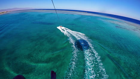 Der-Blick-Nach-Unten-Auf-Einen-Touristen,-Der-Hinter-Einem-Schnellboot-über-Einem-Azurblauen-Ozean-Parasailing-Fährt