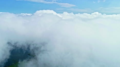 Flying-above-thick-clouds-with-the-peak-on-green-meadows-below