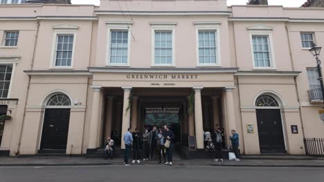 Entrance-to-historic-Greenwich-Market-hall-with-stalls-and-shops-selling-antiques,-art-and-other-goods-as-well-as-street-food-With-Traffic-Going-Past-On-College-Approach-Road