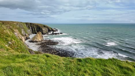 Seascape-incoming-tide-large-seastack-and-lush-green-grass-in-cliff-edge-Copper-Coast-Waterford-Ireland-on-a-spring-afternoon-in-April