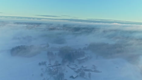 Birdseye-view-over-misty-dew,-aerial-winter-landscape-in-Latvian-village