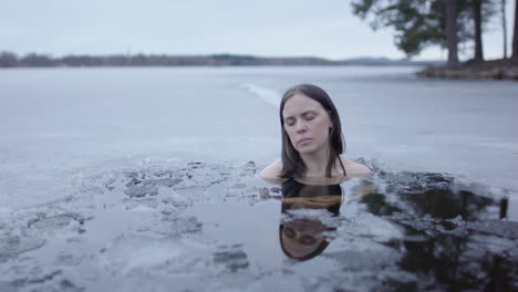 Serene-shot-of-a-beautiful-woman-in-an-ice-cold-lake-at-dusk,-slider-closeup