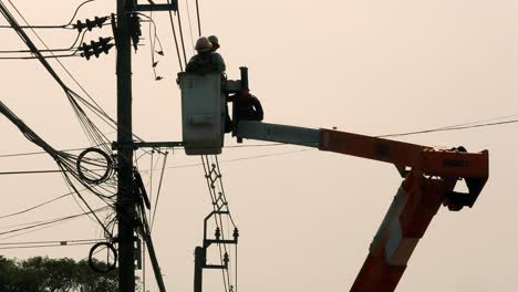 Electric-repairmen-hoisted-on-a-crane-to-reach-the-affected-parts-of-an-electric-wire-and-post-at-a-neighborhood-in-Bangkok,-Thailand