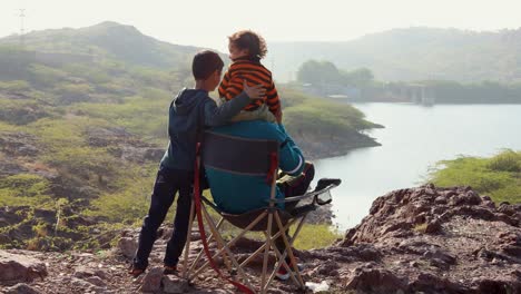 Sohn-Und-Vater-Sitzen-Morgens-Im-Campingstuhl-Auf-Einem-Berggipfel-Mit-Seeblick