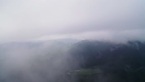Moviéndose-A-Través-De-Una-Densa-Niebla-A-Medida-Que-Se-Eleva-Para-Revelar-Imponentes-Montañas-Y-Exuberantes-Colinas-Verdes.