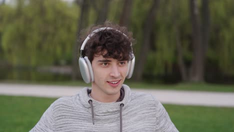Guy-with-curly-hair-use-wireless-headphones-to-listen-music-at-outdoor-park
