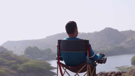 Isolierter-Mann-Sitzt-Morgens-Im-Campingstuhl-Auf-Dem-Berggipfel-Mit-Blick-Auf-Den-See