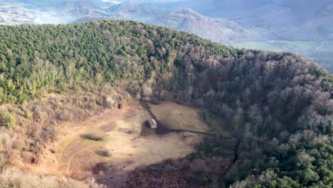 Langsamer-Helix-Kreis-Aus-Der-Luft-Um-Den-Inaktiven-Vulkan-Santa-Margarida:-Riesiger-Krater-Und-Historische-Kapelle-In-Katalonien,-Spanien