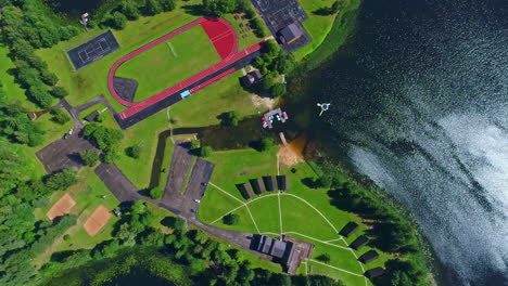 Aerial-View-Of-Silmaci,-Recreation-Complex-With-Courts,-Running-Track-And-Cabins-By-The-Ozero-Lizdole-Lake-In-Latvia