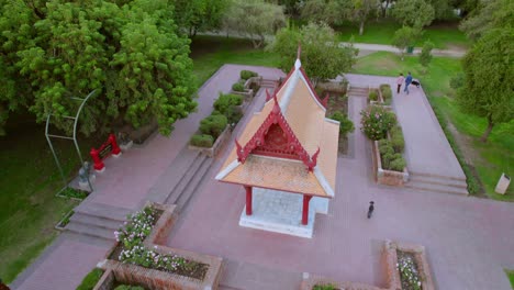 Drone-Aéreo-Volar-Monumento-Plaza-Tailandia-Santiago-Chile-Parque-Verde-Urbano-Con-Senderos,-Peatones-Caminando-Por-Zona-Verde-Con-Horizonte-De-Luz-Natural