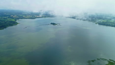 Aerial-drone-panoramic-cloudy-green-lake-foggy-green-rural-village-meadows-in-wet-humid-scenario,-delta-small-town-as-seen-from-above