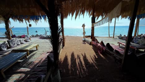 Walk-inside-beach-resort-with-pale-golden-tones-wooden-beach-shoreline-sea-blue-water-of-egypt-dahab-travel-destination-POV