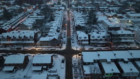 Twilight-over-snow-blanketed-American-city-street,-lined-with-row-houses-and-lit-by-warm-glows