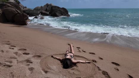 Mujer-Bañada-Por-El-Sol-Haciendo-ángel-De-Arena-En-La-Costa-Tropical-De-Koh-Samui,-Tailandia