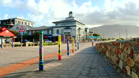 Tourist-strolls-past-colorful-street-art-on-bollards-in-Hermanus-CBD,-Overstrand