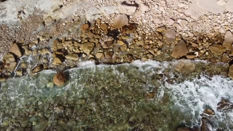 Aerial-Drone-View,-Birds-Eye-looking-down,-Rocky-Mediterranean-Shoreline-in-Calpe,-Spain:-Waves-Crashing-on-Crystal-Clear-Waters