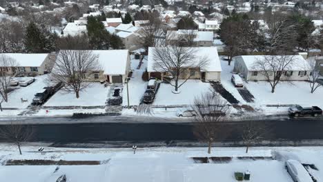 Suburban-street-with-snow,-lined-by-leafless-trees-and-houses-with-driveways,-cars-parked