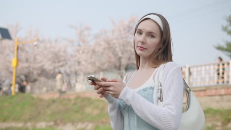 Joven-Viajero-En-El-Parque-Forestal-Ciudadano-De-Yangjae-Usando-Un-Teléfono-Móvil-Mientras-Pasea-Por-El-Distrito-De-Seocho,-Ciudad-De-Seúl,-Corea-Del-Sur