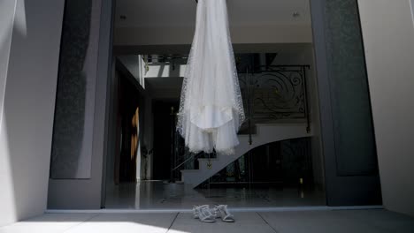 A-wedding-dress-and-her-shoes-hanging-at-the-entrance-to-a-luxurious-house,-the-wedding-is-being-prepared