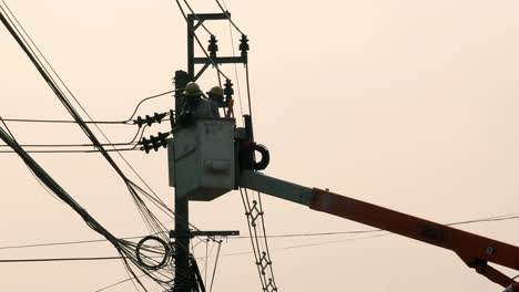 Two-electricians-wearing-hard-hats,-in-a-railed-aerial-platform,-attached-to-a-hydraulic-crane-or-a-boom-lift,-are-being-lowered,-Bangkok,-Thailand