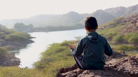 Isolierter-Kleiner-Junge,-Der-Morgens-Auf-Einem-Berggipfel-Yoga-Praktiziert-Und-Seeblick-Hat