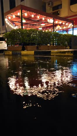On-a-rainy-night,-restaurant-lights-reflect-in-the-rainwater,-creating-a-mesmerising-scene