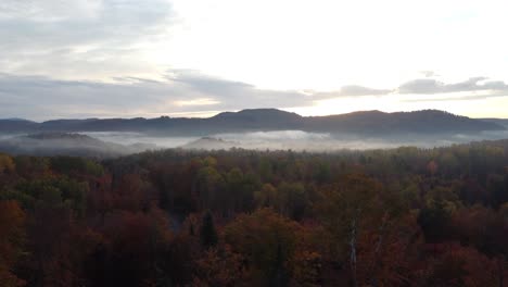 Vista-Aérea-Del-Paisaje-Forestal-Brumoso-De-La-Mañana-Con-Picos-Montañosos-Y-Paisaje-Místico-Mágico-Del-Sol