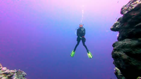 Scuba-diver-floats-between-cliffs-underwater-blue-sea-ocean-in-trip-at-egypt-dahab,-water-exploration-around-oceanic-floor