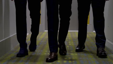 Close-ups-of-the-legs-and-shoes-of-three-men-walking-down-a-hotel-corridor,-they-are-dressed-in-suits