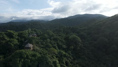 Drone-pans-up-from-the-prehistoric-beach-boulders-to-reveal-the-mountains-and-rainforest-of-Tayrona,-in-Colombia,-as-the-sun-sets-in-the-background