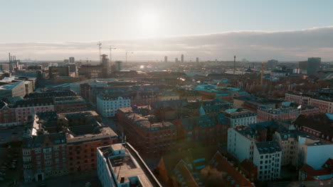 Bewegte-Drohnenaufnahme-Der-Skyline-Der-Innenstadt-Von-Kopenhagen-Mit-Vorbeifahrenden-Autos-Und-Baukränen-Im-Hintergrund
