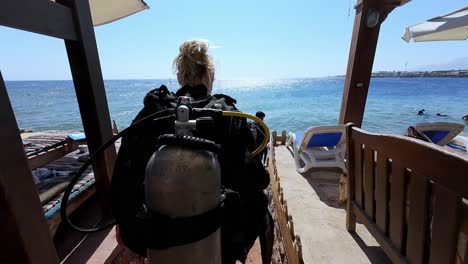 Woman-walk-inside-beach-resorts-with-white-umbrellas,-diving-scuba-spot-at-egypt-dahab-waterfront,-divers-go-to-the-sea,-perspective