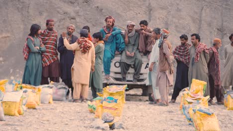 Group-Of-Locals-Standing-Near-Truck-Beside-Rows-Of-Food-Distribution-Aid-Sacks-On-The-Ground-In-Balochistan