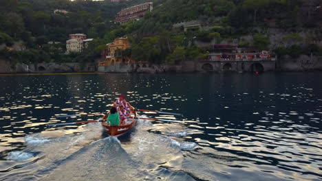 Drone-shot-passing-a-rowing-boat-team,-practicing-on-the-sea,-sunset-in-Italy