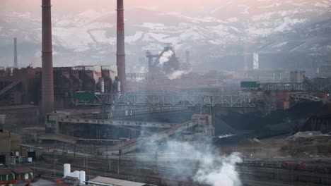 La-Luz-Del-Amanecer-Ilumina-Un-Amplio-Sitio-Industrial-Con-Chimeneas-Y-Transportadores,-Enmarcado-Por-Un-Escarpado-Telón-De-Fondo-Montañoso.