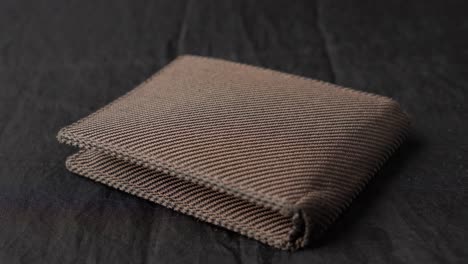 Hand-Laying-Placing-Brown-Fabric-Wallet-On-Black-Cloth,-Close-Up