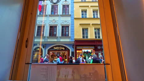 View-from-a-window-onto-colorful-storefronts-in-Prague-and-tourists-exploring-the-city