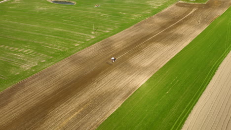 A-tractor-creates-contrasting-stripes-on-a-vast,-green-field,-showcasing-precision-agriculture-from-an-aerial-perspective