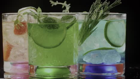 Glasses-swirling-with-vibrant,-multi-colored-drinks,-infused-with-the-refreshing-zest-of-lemon-mint,-set-against-a-sleek-black-backdrop